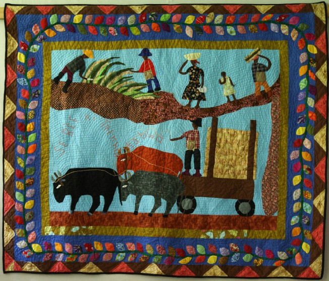 Quilt artist Denise Estavat tells the story of life in the village where she grew up.  The men cut sugar cane and the oxen pull the cart to deliver it to market.  Notice the intense echo quilting and refined details in embroidery.